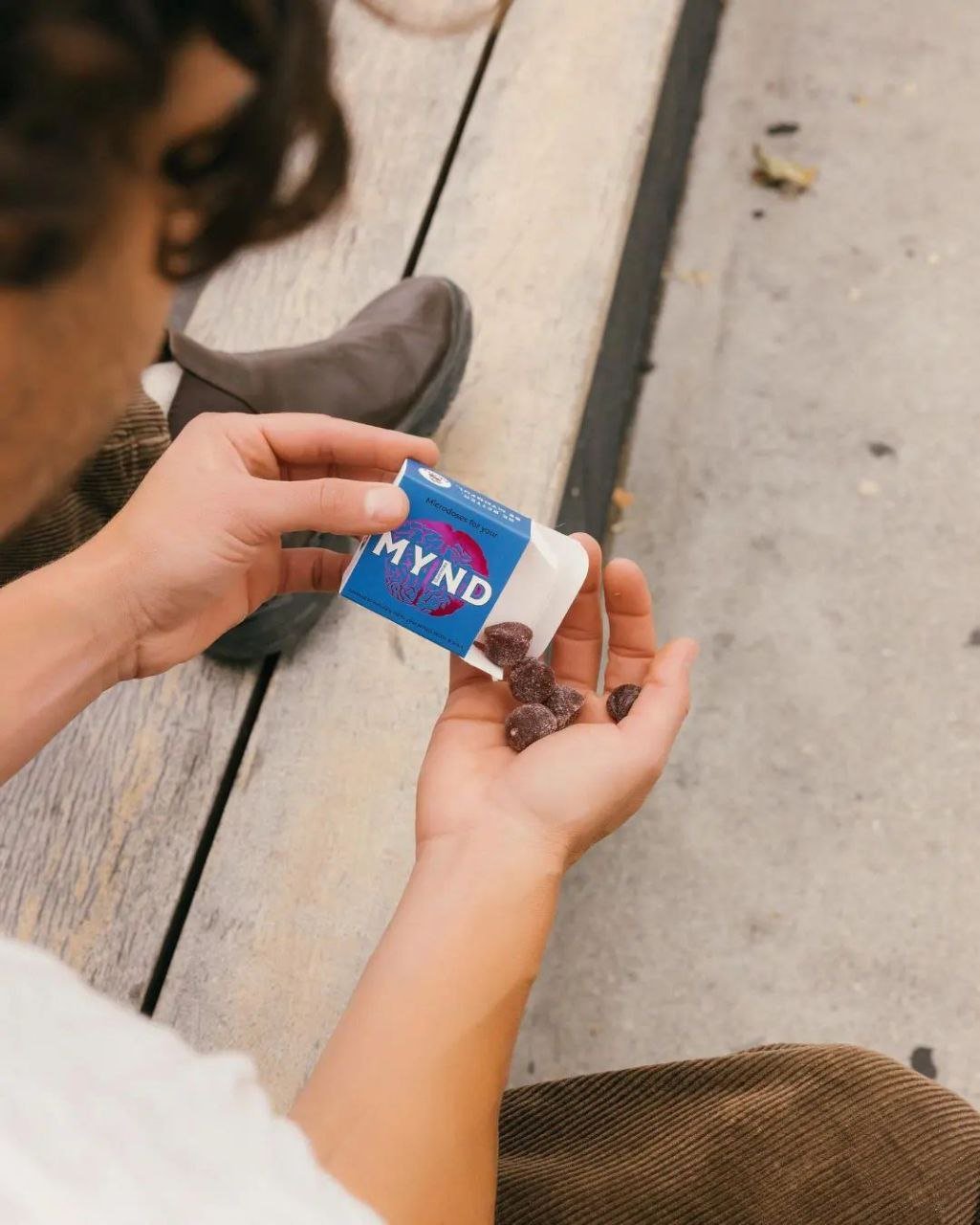 Man sitting on a wooden bench pouring delicious mindfully crafted mushroom gummies onto his palm from a mynd mushroom gummy packet